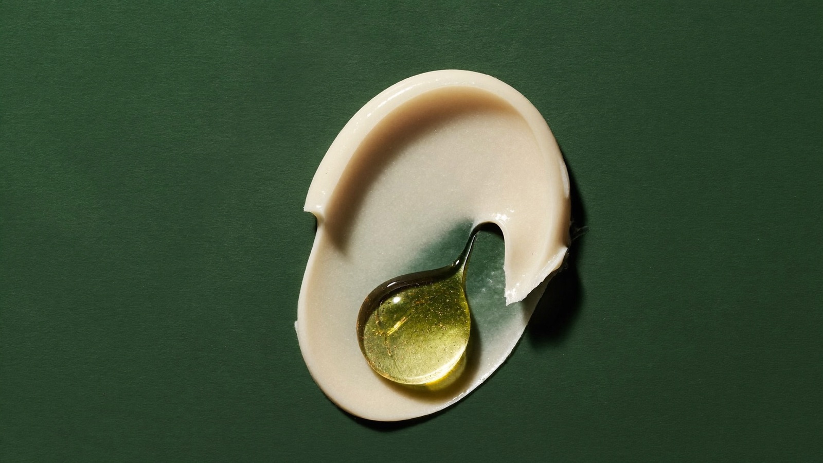 Texture di crema con una goccia di olio ambrato su superficie verde